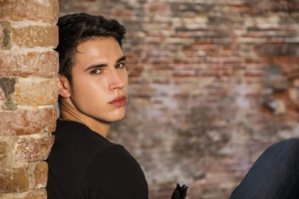 Attractive young man sitting against brick wall — Stock Photo, Image