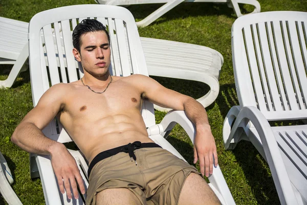 Без рубашки молодой человек, загорая в шезлонге на траве — стоковое фото