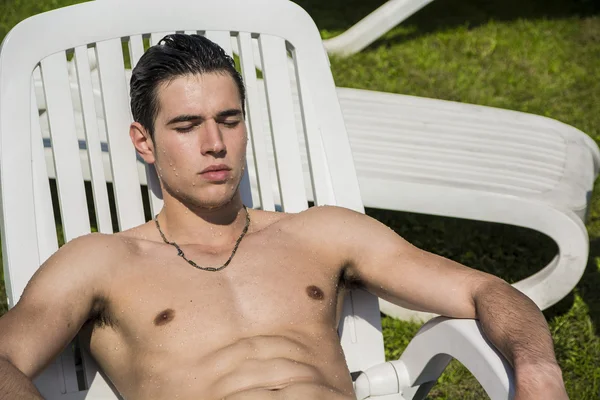 Jovem sem camisa tomando sol na espreguiçadeira na grama — Fotografia de Stock