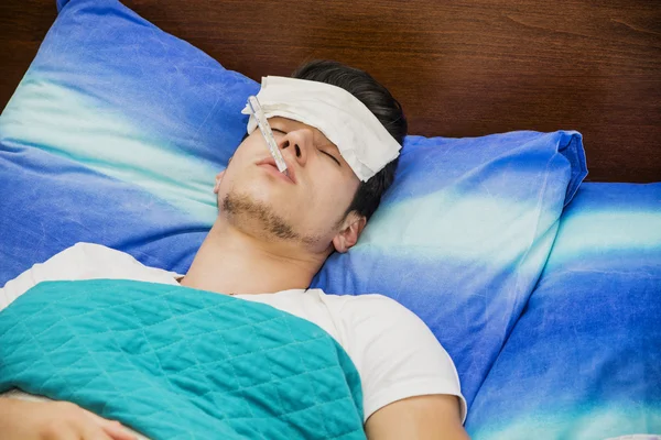 Jonge man in bed meten koorts met thermometer — Stockfoto