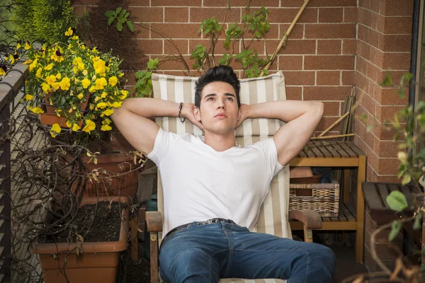 Handsome young man in balcony day-dreaming, sitting on chair — Stock Photo, Image