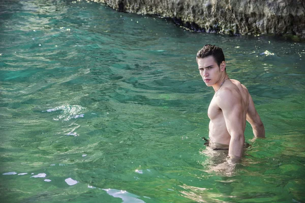 Young shirtless athletic man standing in water by ocean shore — Stock Photo, Image