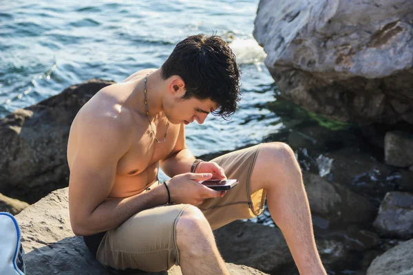 Zaneprázdněný muž s jeho telefon sedí na Beach Boulders — Stock fotografie