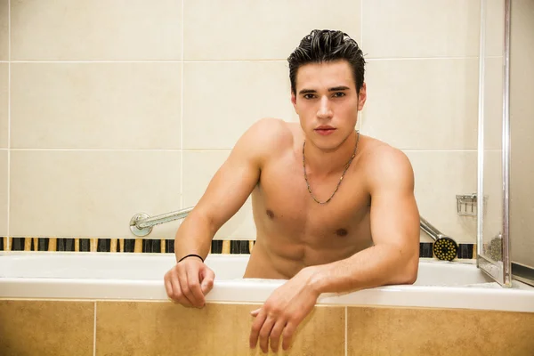 Красивый молодой человек в ванной дома принимает ванну — стоковое фото