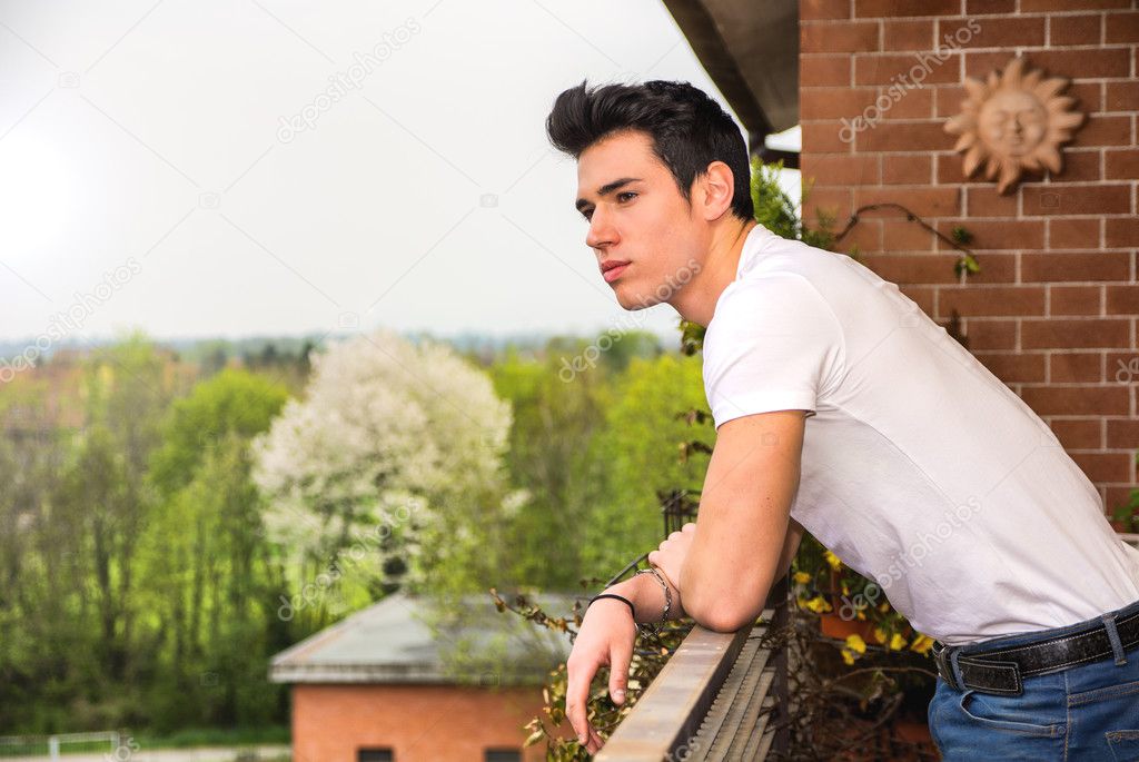 Handsome dark haired young man looking out on balcony
