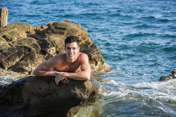 Jeune homme torse nu athlétique appuyé sur la roche par la mer — Photo