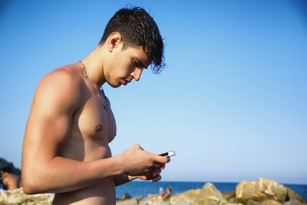Kullanarak cep telefonu plaj kayalar duran genç adam — Stok fotoğraf