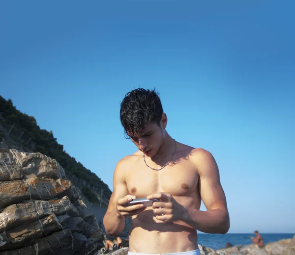 Hombre joven de teléfono celular utilizando en cantos rodados de playa — Foto de Stock