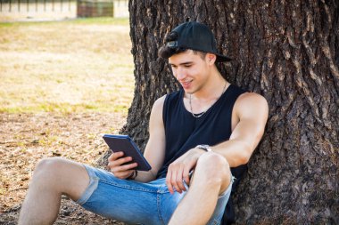 Young Man with Tablet or Ebook Reader Relaxing at Park