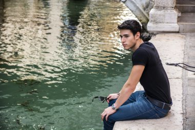 Young Man Sitting Next to Canal in Venice, Italy