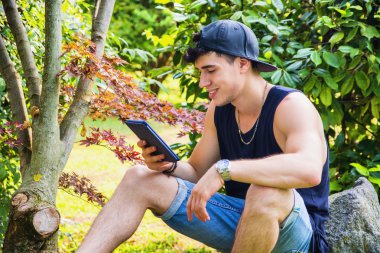 Young Man with Tablet or Ebook Reader Relaxing at Park