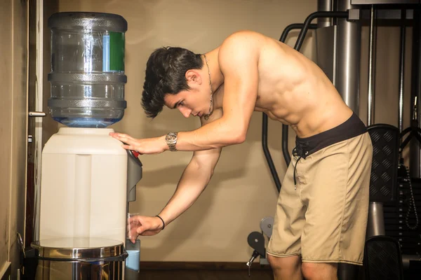 Attractive athletic young man drinking water in gym — kuvapankkivalokuva