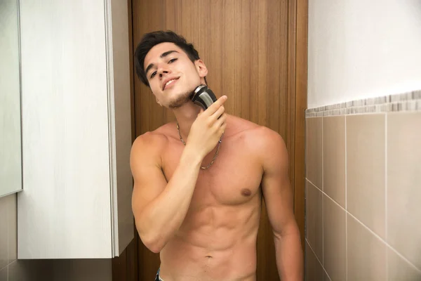 Muscular man shirtless using electric shaver, looking at camera — 图库照片