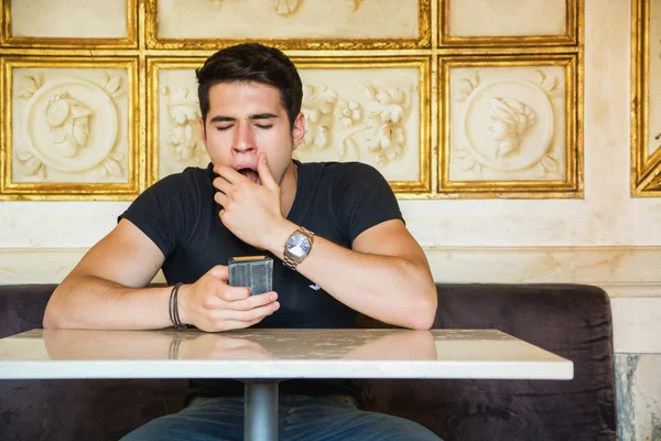 Bored young man yawning while using cell phone —  Fotos de Stock