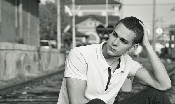 Attractive young man sitting on railroad smiling — Stok fotoğraf