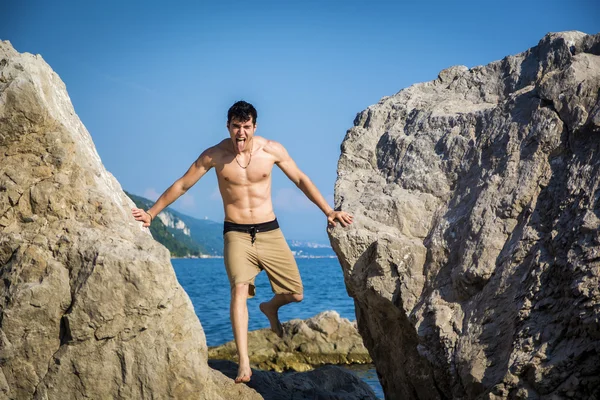 Mladý muž Spanning propast mezi pobřežní balvany — Stock fotografie
