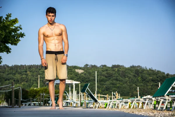 Молодой человек без рубашки спортивная(ый), стоя на пляже — стоковое фото