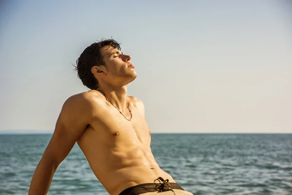 Smiling young man sitting by sea or ocean shore sunbathing — Stock Photo, Image