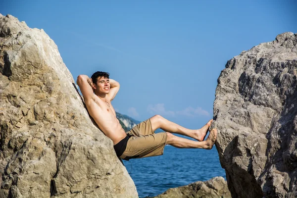Mladý muž Spanning propast mezi pobřežní balvany — Stock fotografie