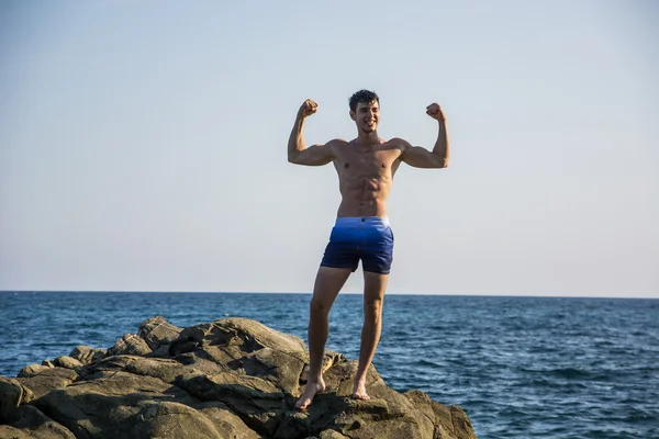 Muscular young man on rock by sea — Stock Photo, Image