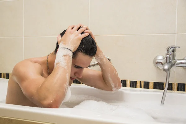 Красивый молодой человек в ванной дома принимает ванну — стоковое фото