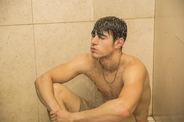 Грустно молодой человек принимает душ, сидя на полу — стоковое фото