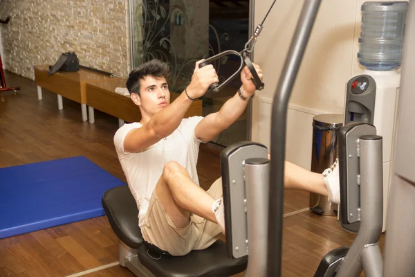 Handsome young man working out on gym equipment — Stock Photo, Image