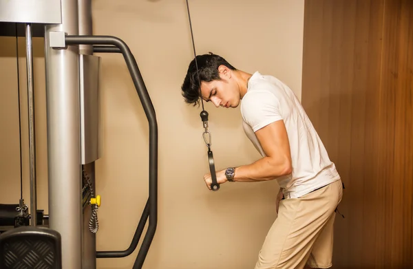 Handsome young man working out on gym equipment — Stock Photo, Image