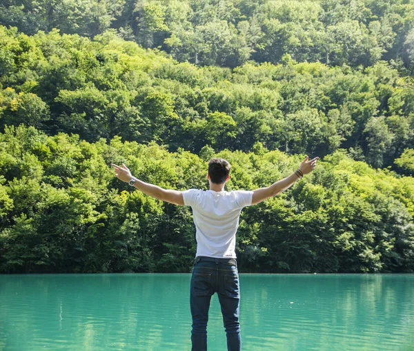 Young man, arms spread open enjoying freedom in front of lake — Stock Photo, Image