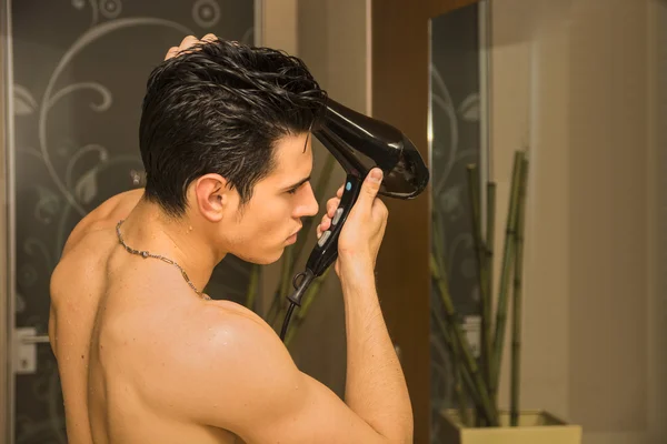 Jovem sem camisa secando o cabelo com secador de cabelo — Fotografia de Stock