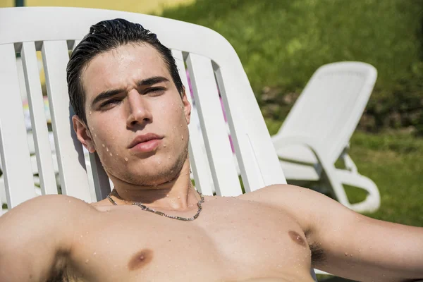 Jovem sem camisa tomando sol na espreguiçadeira na grama — Fotografia de Stock
