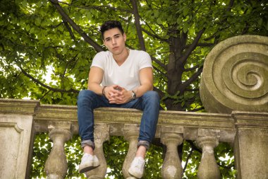 Handsome young man sitting on a balcony or bridge