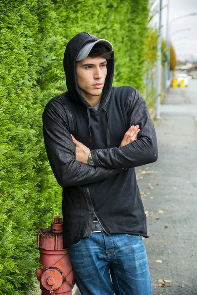Jovem bonito na camisola de capuz preto, em pé ao ar livre Imagem De Stock