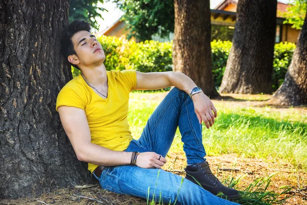 Jovem atraente no parque descansando contra a árvore — Fotografia de Stock