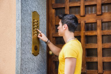 Young man ringing doorbell and talking on speaker phone