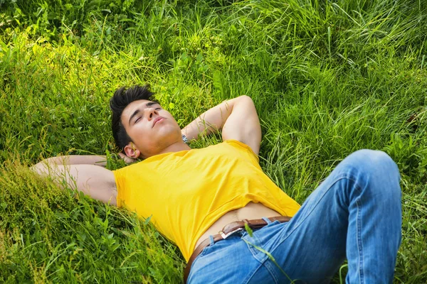 Jovem bonito apto relaxantes deitado no gramado — Fotografia de Stock