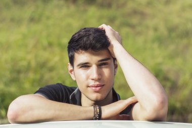 Young man looking at camera outdoor, leaning with head resting on hands