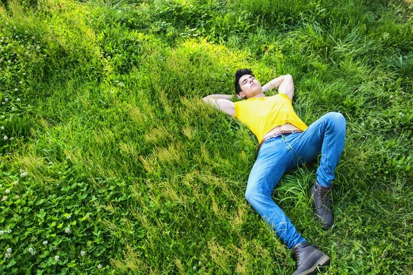 Jovem bonito apto relaxantes deitado no gramado — Fotografia de Stock