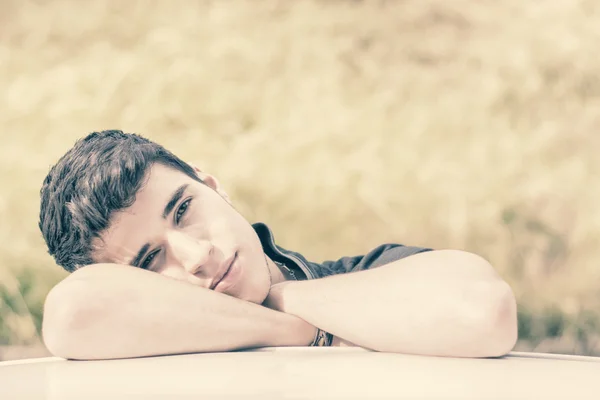 Young man looking at camera outdoor, leaning with head resting on hands — Stok fotoğraf