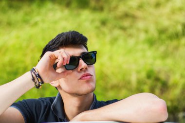 Young man looking at camera outdoor, leaning with head resting on hands
