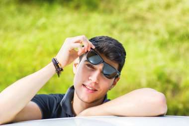 Young man looking at camera outdoor, leaning with head resting on hands