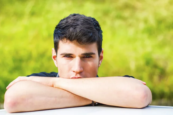 Young man looking at camera outdoor, leaning with head resting on hands — Stok fotoğraf