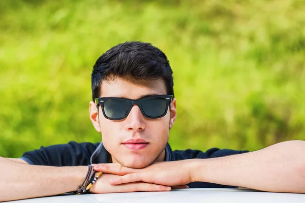 Young man looking at camera outdoor, leaning with head resting on hands — Stockfoto
