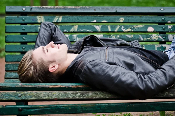 Attraktive blauäugigen, blonden jungen Mann Verlegung auf Parkbank — Stockfoto