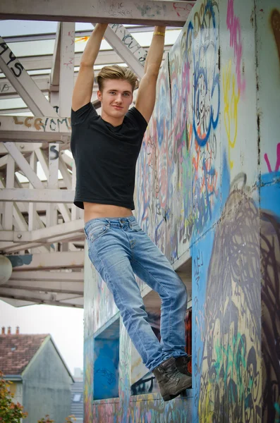 Handsome blond young man hanging from concrete structure — Stock Photo, Image