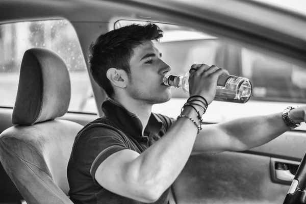 Молодой человек водит свою машину, когда пьет алкоголь — стоковое фото