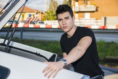 Young man taking luggage and bag out of car trunk