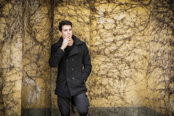 Schöner junger Mann stehend gegen Mauer Pflanzen bedeckt — Stockfoto