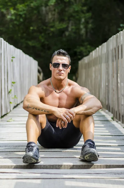 Bello, serio muscleman seduto contro il recinto in legno — Foto Stock