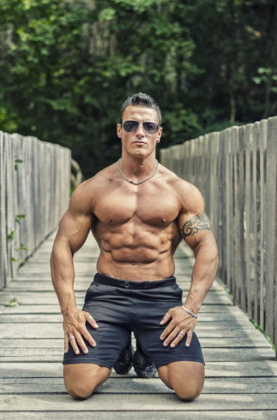 Przystojny, poważne muscleman siedząc przed ogrodzenia z drewna — Zdjęcie stockowe